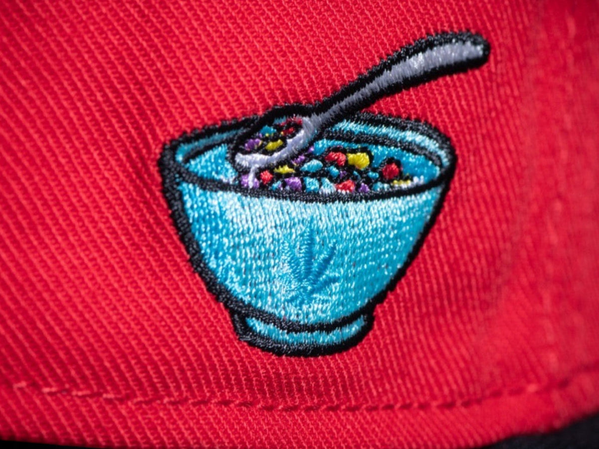 Gorra snapback roja CAYLER & SONS con bordado lateral de un tazón de cereales colorido y estilo urbano